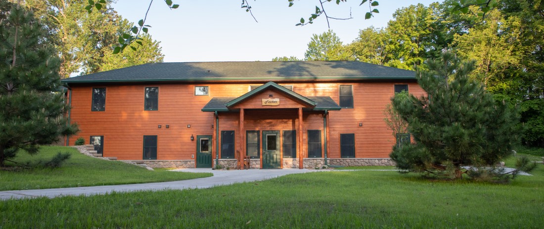 Two story cabin-style building, surrounded by trees with a sidewalk leading to the front door
