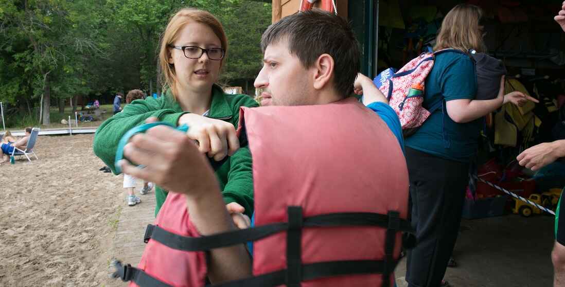 Counselor helping camper put on lifejacket.