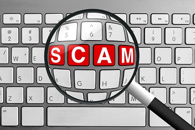 white keyboard with magnifying glass enhancing the word "scam" in red letters