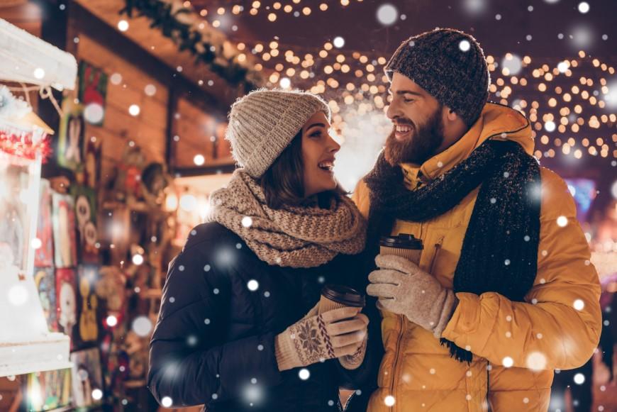 Smiling couple in holiday scene outside holding warm beverages