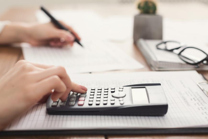 Hands of an individual using a calculator and writing notes