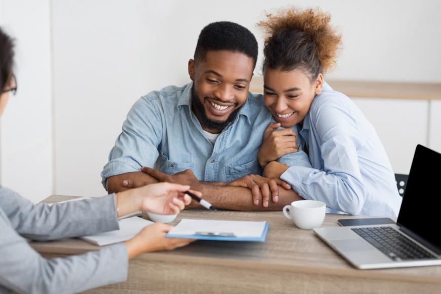 Happy African American couple looking at papers from woman assisting them