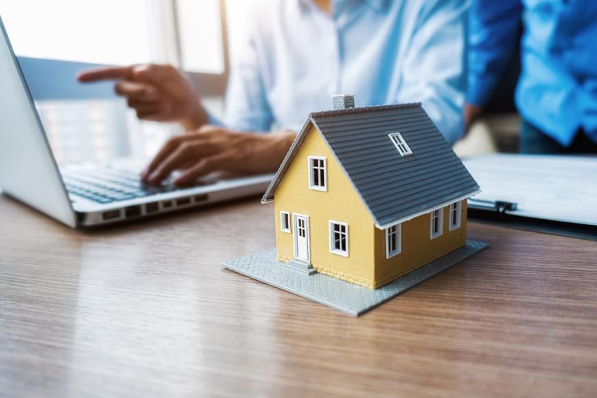 couple working at laptop with miniature of a house next to the laptop
