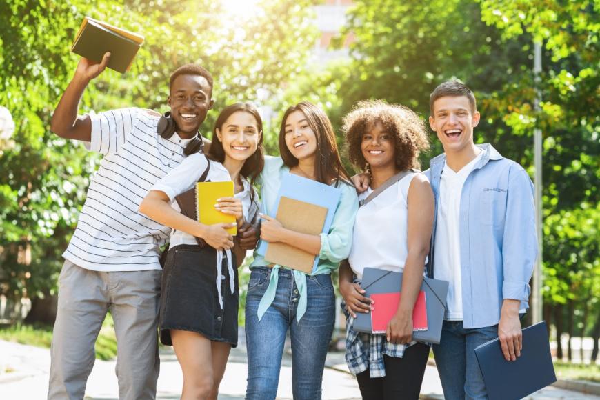 Multiracial group of five college students with their arms around each other and smiling for the camera