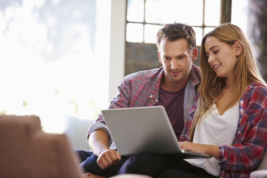 Young woman showing young man her laptop screen. Both of them look at screen with interest