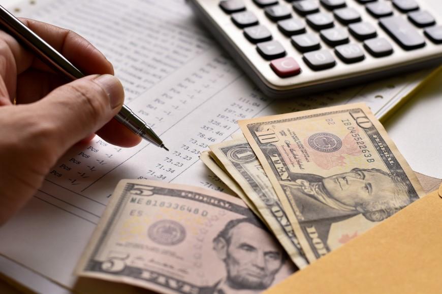 Hand holding pen, money in an envelope, and a calculator