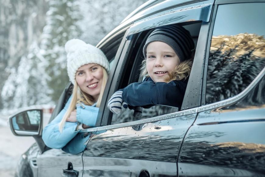Young woman and child looking at camera from open car windows during winter months