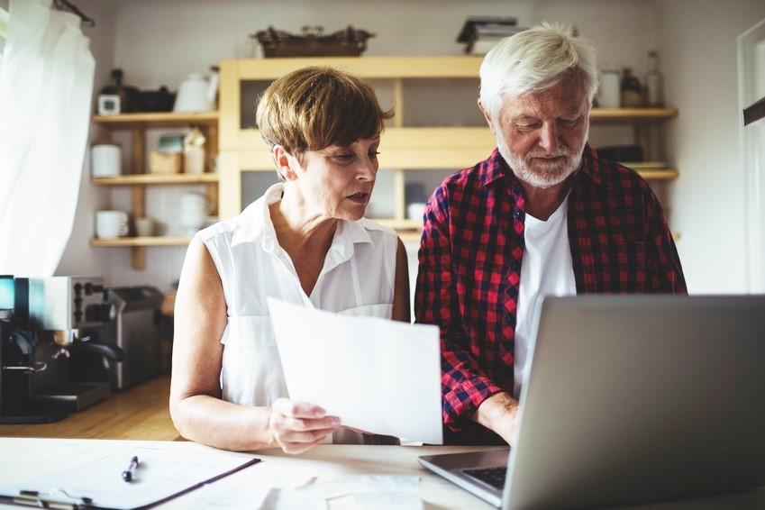 Two older adults reviewing papers and working at a laptop