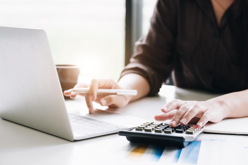 Woman typing on a calculator and working at a laptop