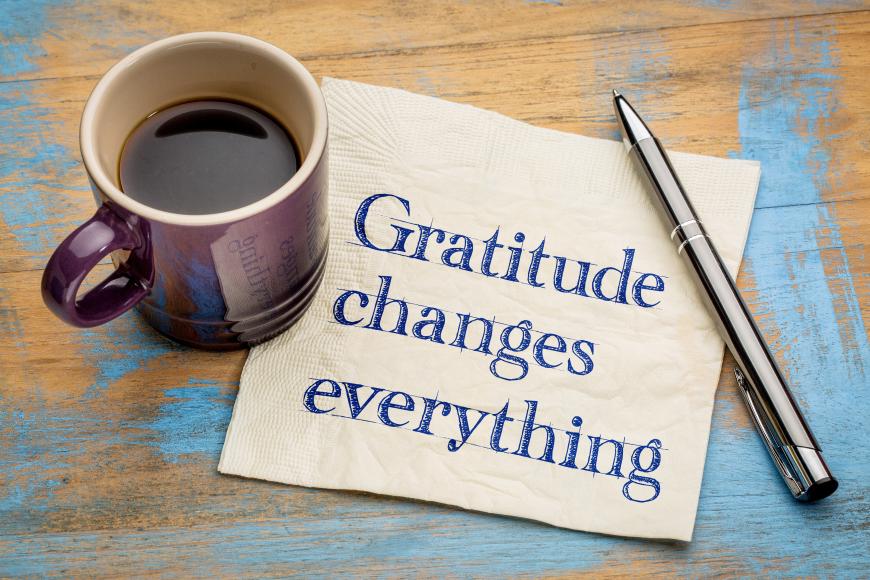 Words on post it note: Gratitude Chnages Everything. Cup of coffee and pen next to post-it note.