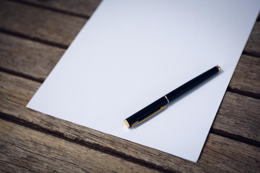 Pen lies on a note pad that is lying on a hard surface.