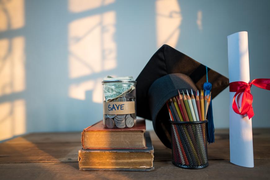 Jar with money on top of two books. To their right is a graduation cap, a container with pencils, and a diploma.