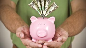 Man's holding a pink piggy bank with bills sticking out of the coin hole