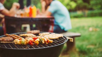 Family at a picnic table with meat cooking on a grill