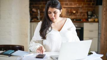 Younger woman at table using calculator and laptop