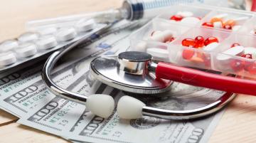 Stethoscope, pills, and syringe lying on $100 bills