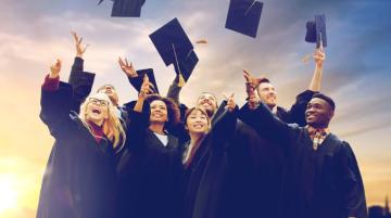 Multiracial group of college grads in graduation gowns celebating and throwing their mortar boards in the air