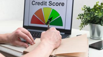 Credit Score graphic n laptop screen, individual writing in notebook in front of laptop