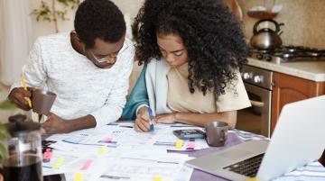 Couple doing calculations at kitchen table.  Many papers spread over the table.