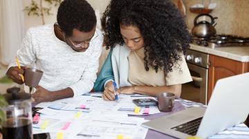 Black couple sitting together and making calculations at a kitchen table covered with papers