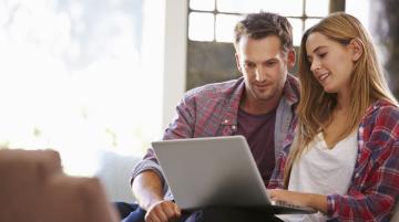 Young woman showing young man her laptop screen.  Both of them look at screen with interest