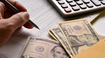 Hand holding pen, money in an envelope, and a calculator