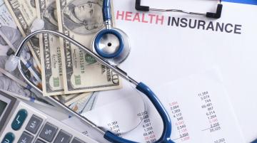 Stethoscope on top of ten-dollar bills and health insurance paperwork