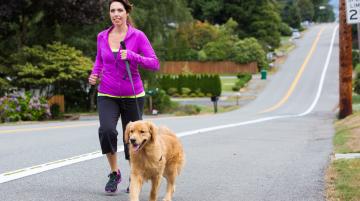 Woman jogging with a dog on a paved road