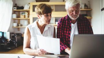 Two older adults reviewing papers and working at a laptop