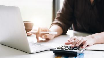 Woman typing on a calculator and working at a laptop