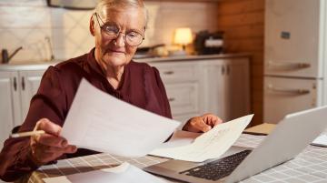Older man sitting in front of his laptop, looking over paperwork
