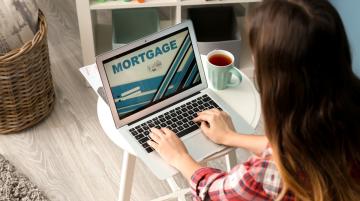 Woman with long reddish hair typing on her laptop. The top of laptop displays the word Mortgage.