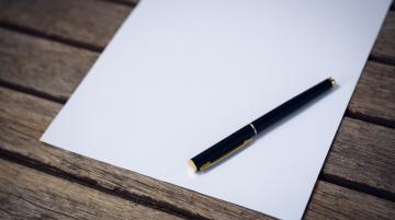 Pen lies on a note pad that is lying on a hard surface.