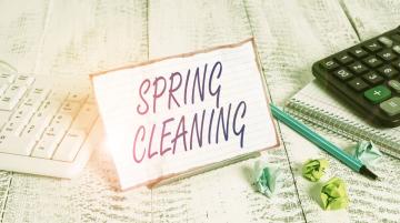 A note with the words SPRING CLEANING.  To the left of the note is a white keyboard.  To the right of the note are a pen; a black calculator; a spiral notebook; and small, crumpled post-it notes of different colors.