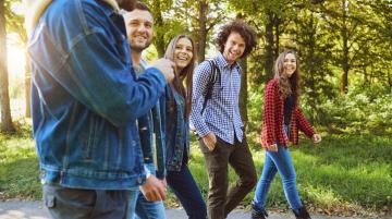Three adult men and two adult women walking and laughing together along a path in a wooded area.