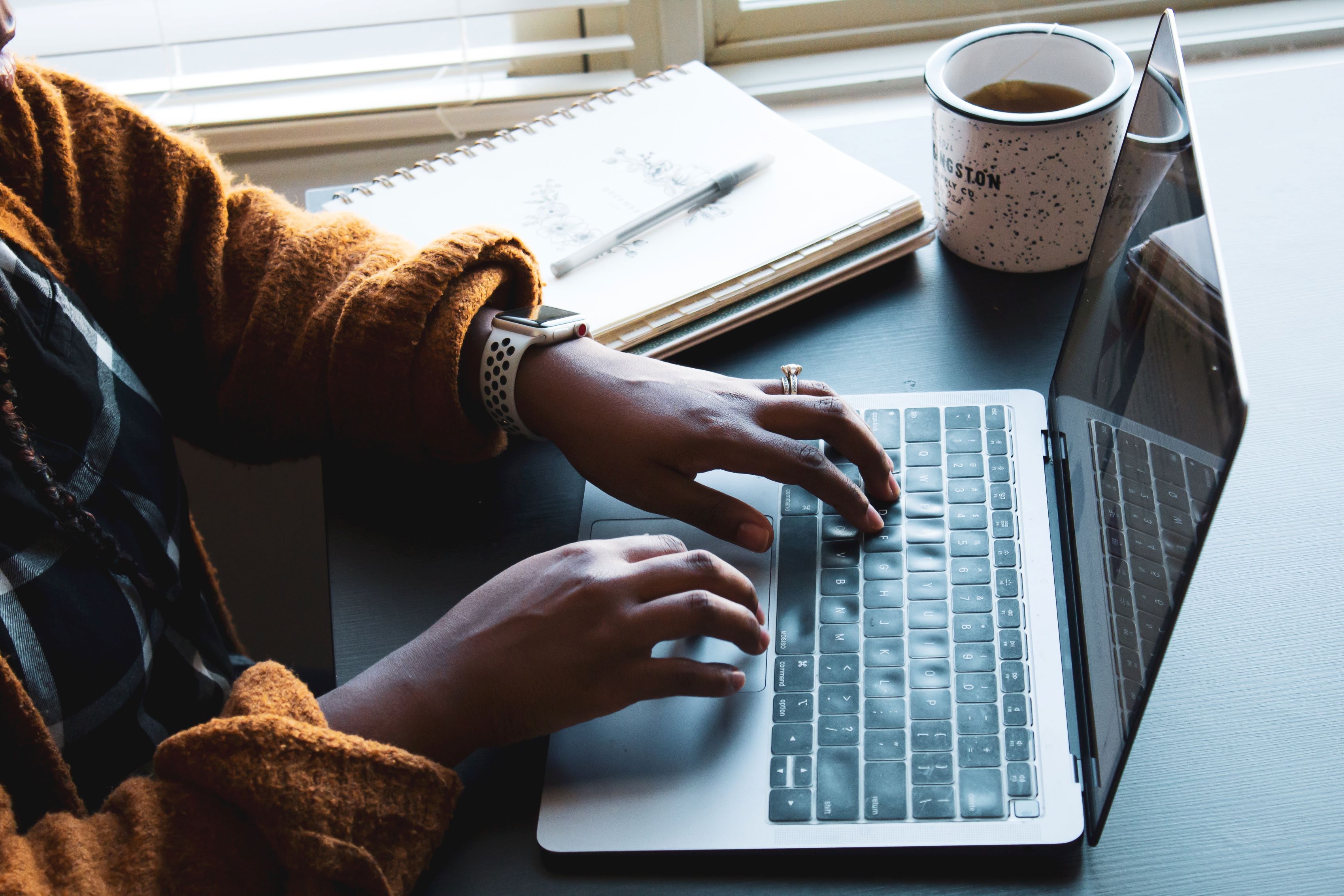 Person typing at a laptop with a notebook and pencil