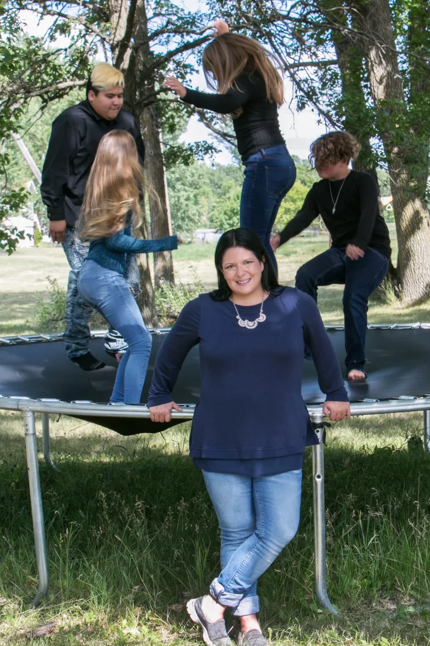Kids jumping on a trampoline. Mom standing in front of the trampoline.