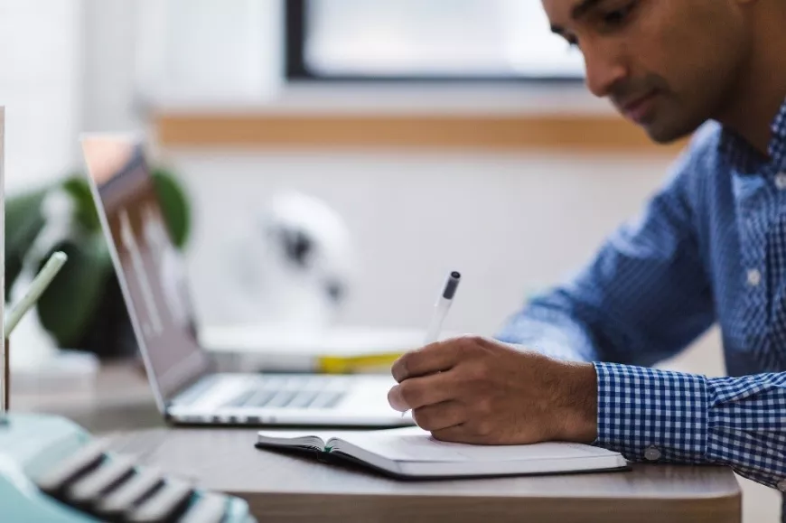 A person writing in a notebook, sitting at a desk