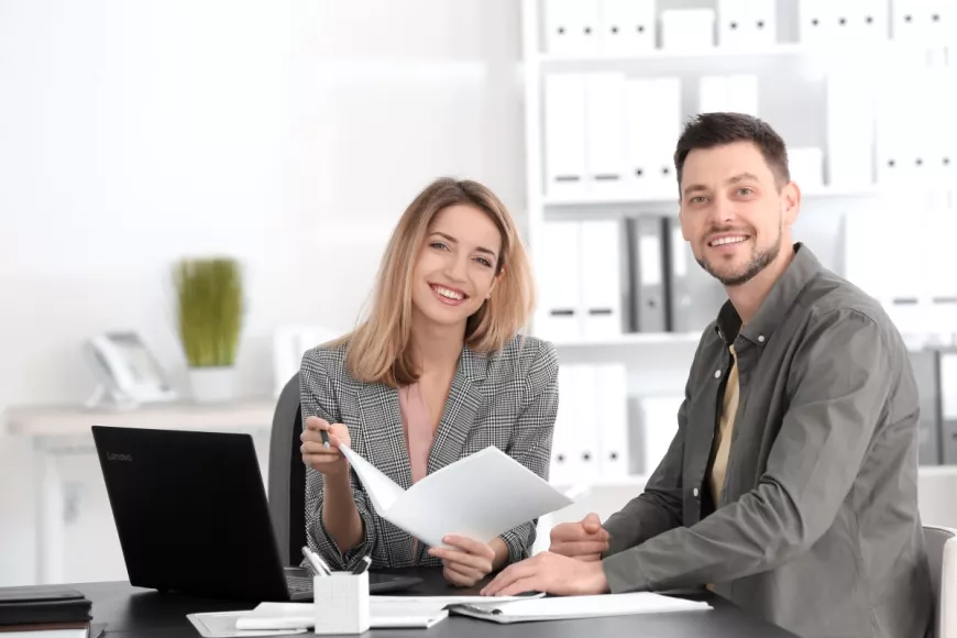 Young adult woman showing young adult man a brochure. Both are smiling at the camera.